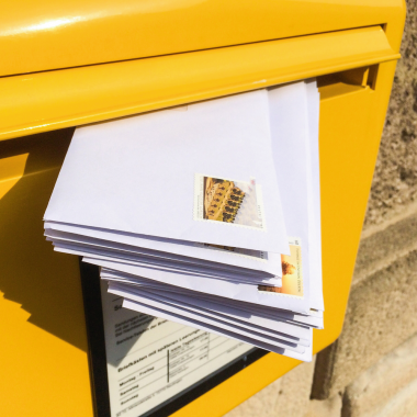 gelber Briefkasten mit einem Stapel frankierter Briefe